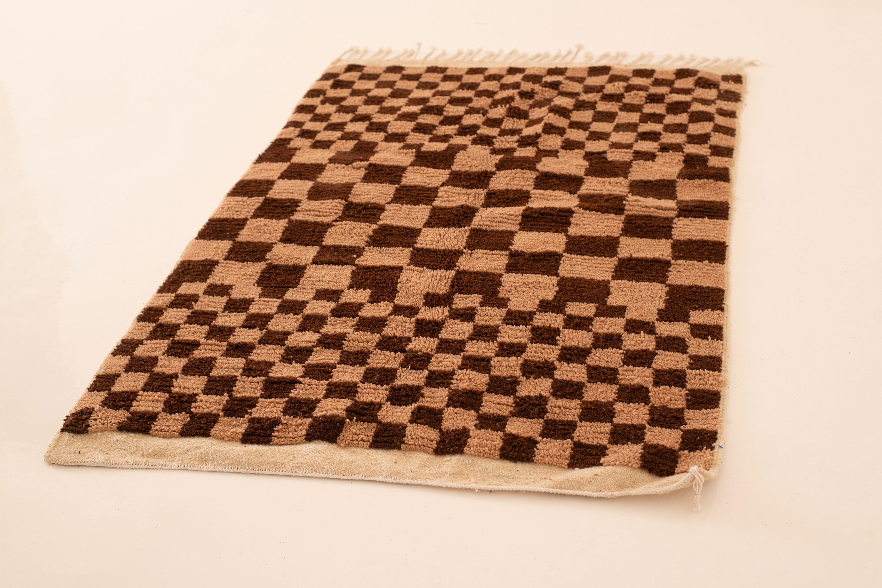 Brown checkerboard patterned rug with fringe edges, perfect for home decor and comfort.