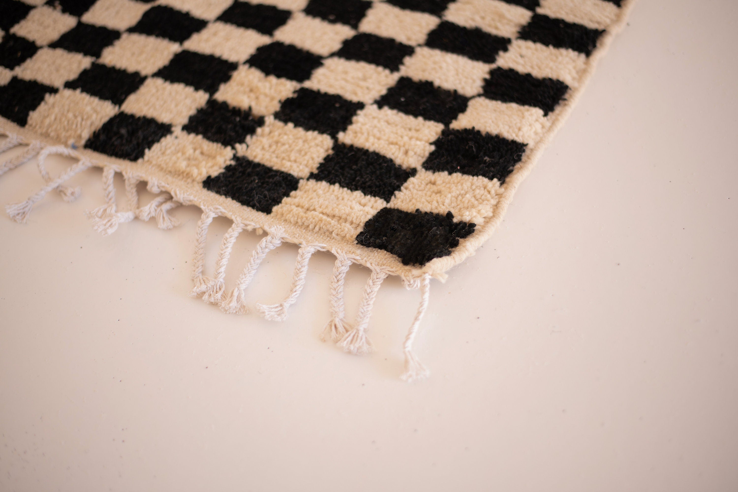 Black and beige checkered rug with fringes, perfect for enhancing home decor styles.