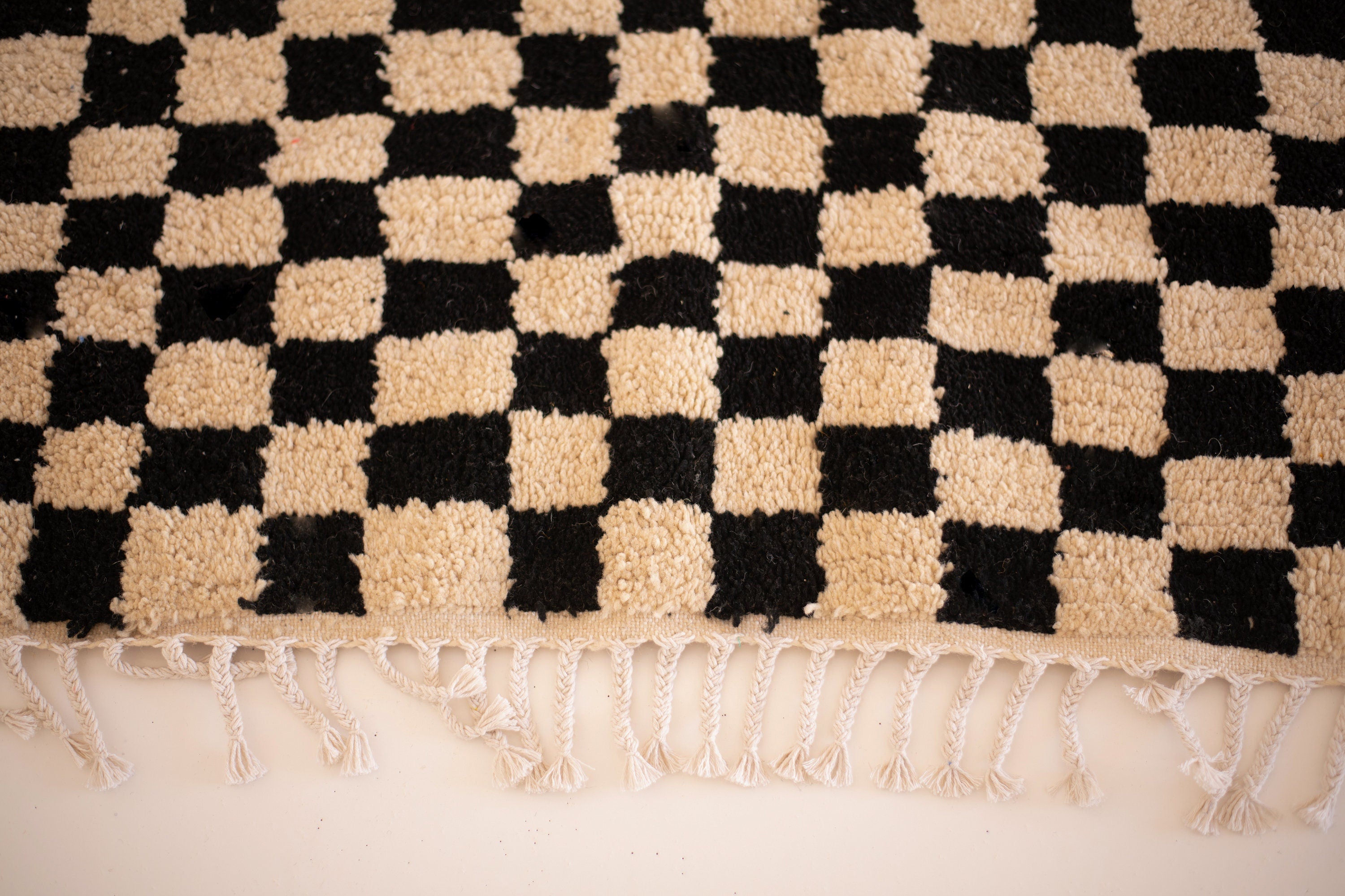 Black and beige checkered rug with fringe detailing, perfect for home decor.