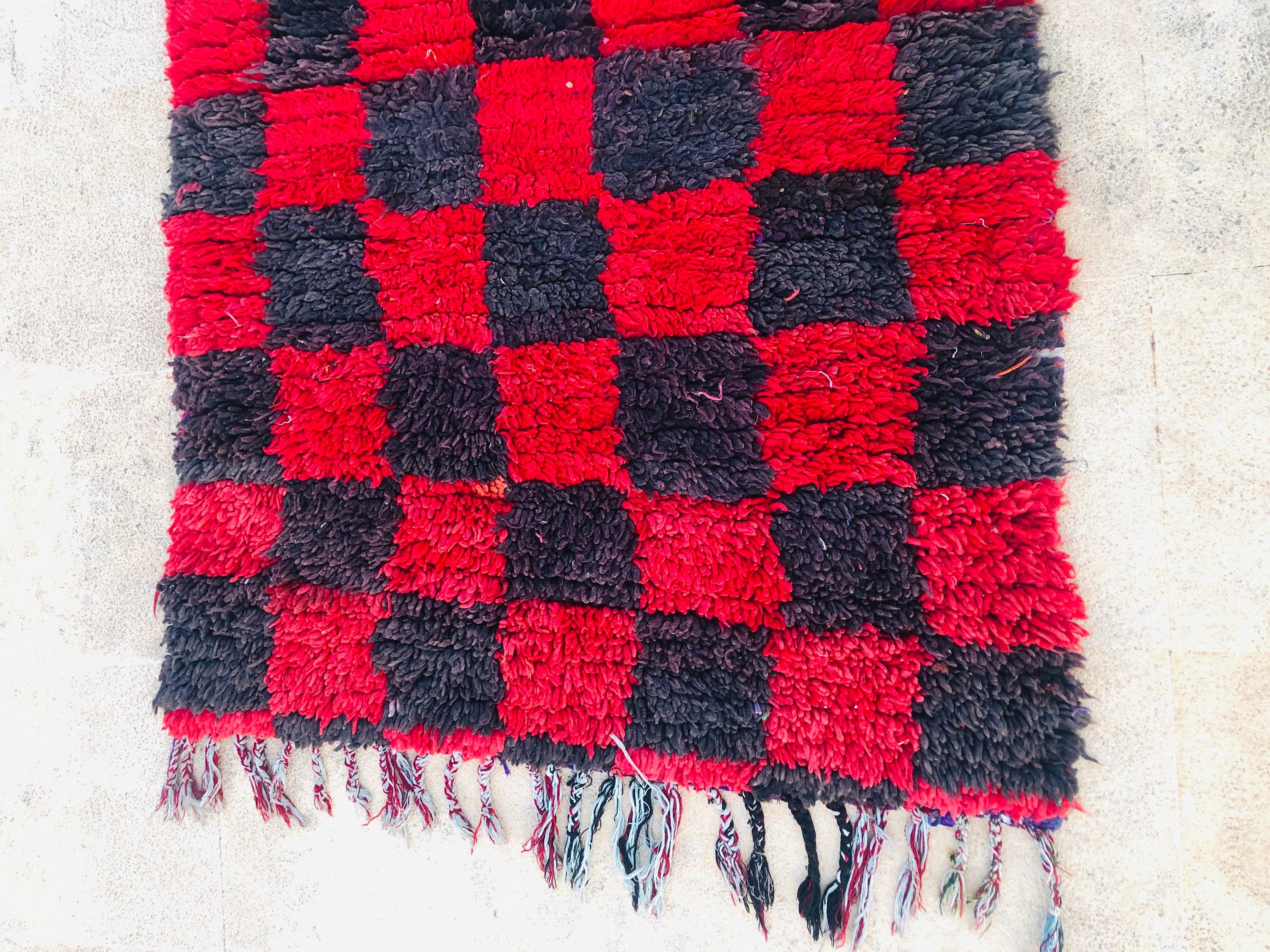 Red and black checkered rug with fringes, perfect for home decor and cozy spaces.