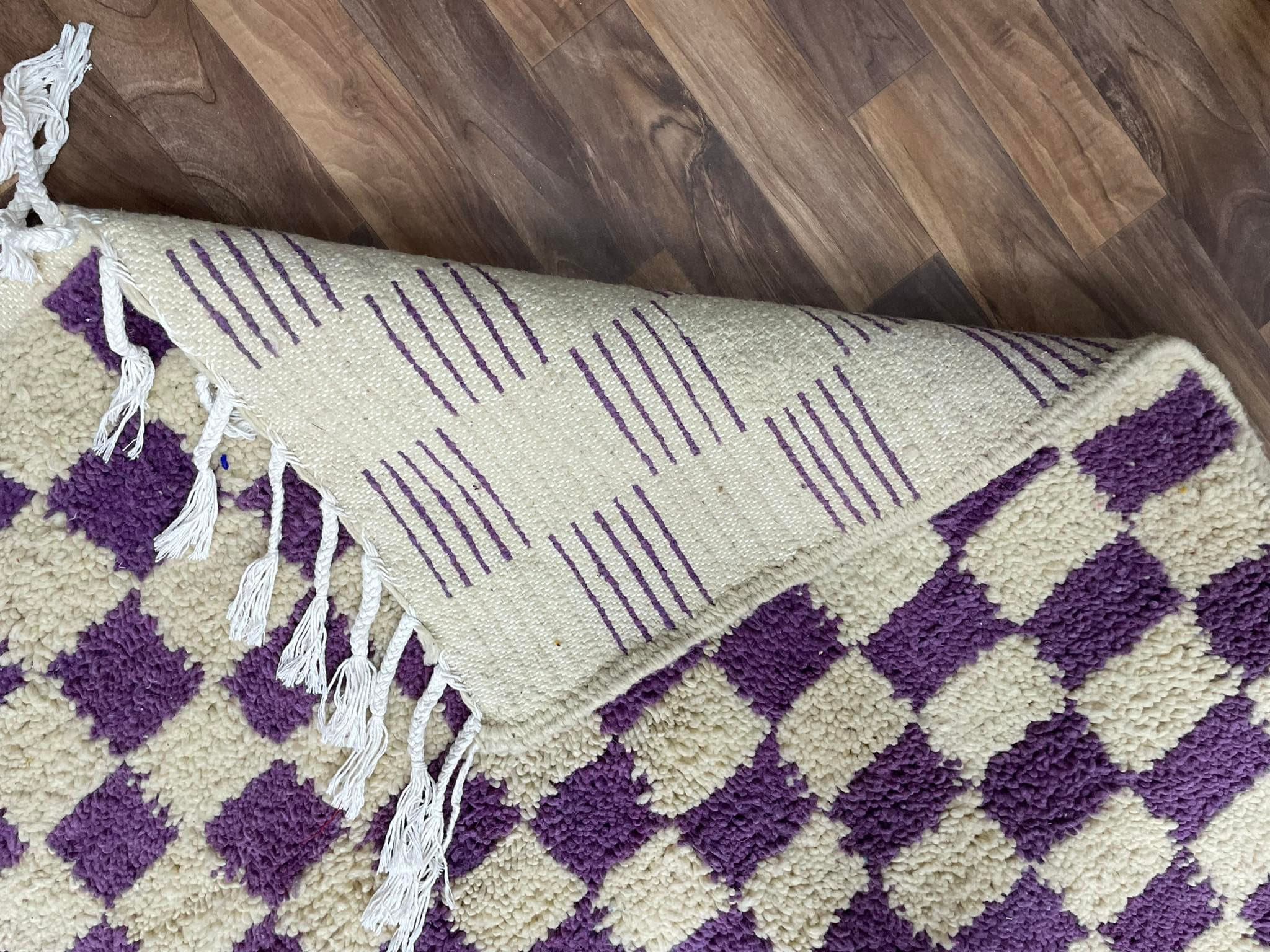 Handwoven purple and cream patterned rug with fringes, perfect for home decor.